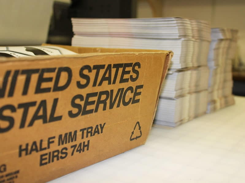 Multiples stacks of mailers next to a USPS shipping box