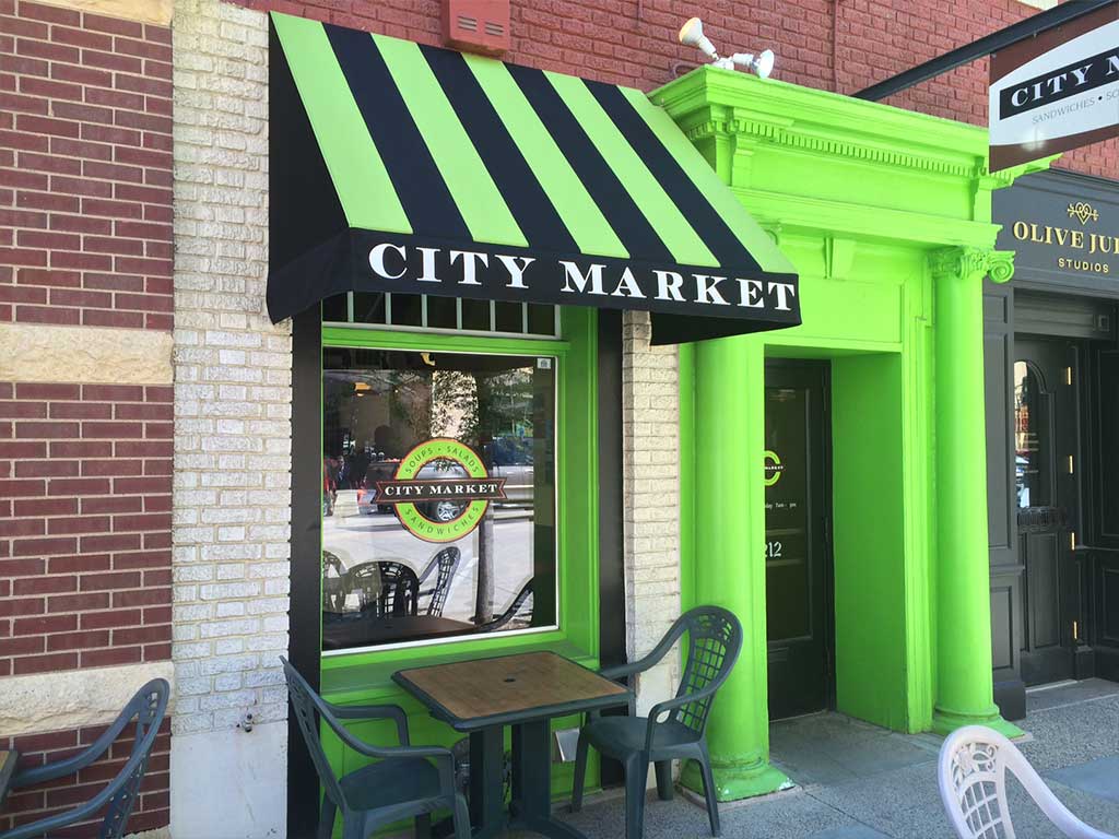 Eye-catching black and green striped fabric awning with bold white lettering, perfect for enhancing storefront visibility and curb appeal.